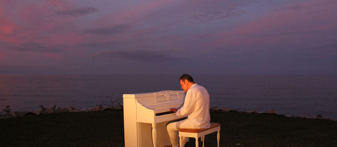Robert Koziel playing a white piano at dusk